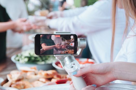 A person uses a smartphone gimbal to film a food event with various dishes.