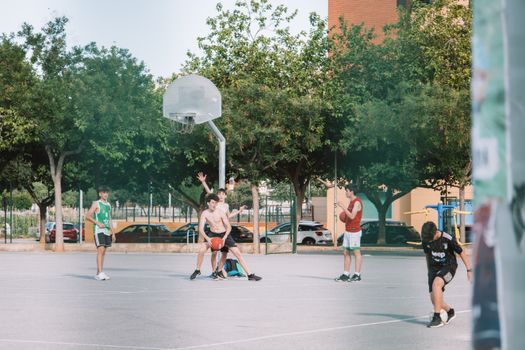 A group of teenagers enjoy a summer basketball game on an outdoor court in Valencia, Spain.