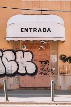 Graffiti-covered facade with 'Entrada' awning in Valencia, Spain.