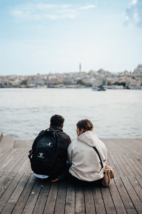 Couple Sitting on the Pier and Looking at the View of City and Sea 