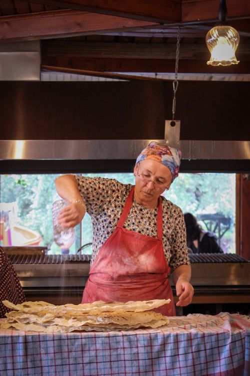 Free A senior woman in a kitchen prepares traditional bread, sprinkling flour on dough. Stock Photo