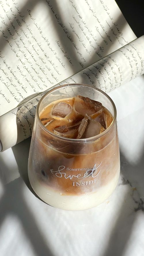 Free A glass of iced coffee on a table with Arabic calligraphy backdrop, capturing warmth and tranquility. Stock Photo