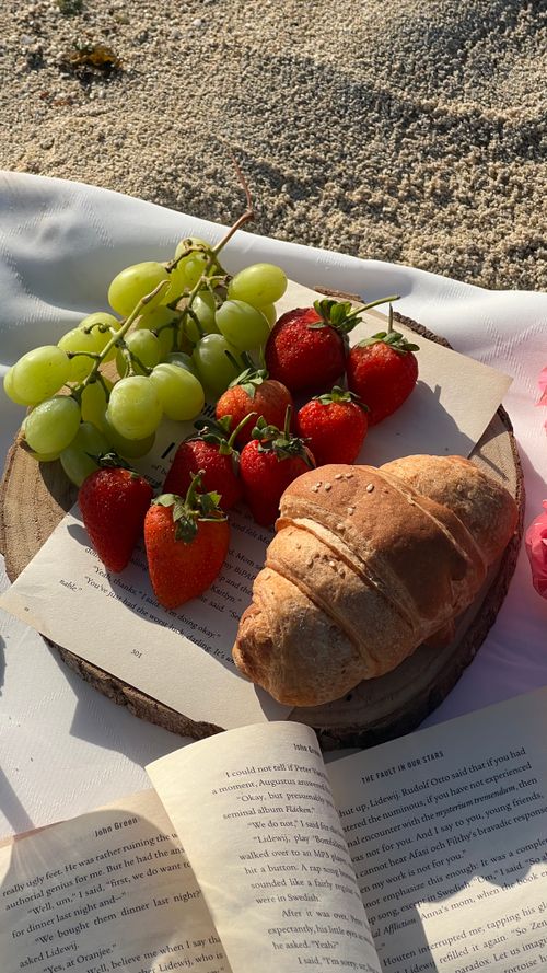 Free Spring picnic setup featuring a croissant, strawberries, and grapes on a rustic tray. Stock Photo