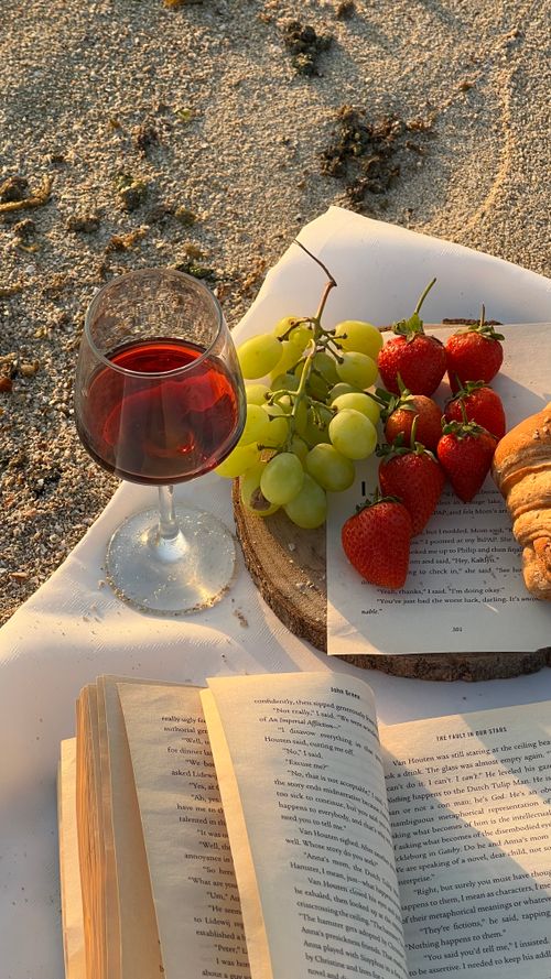 Free A serene beach picnic setup with wine, grapes, strawberries, and an open book. Stock Photo