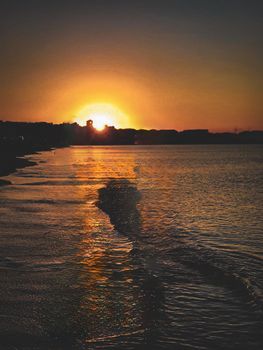 Golden sunset lights the shore with gentle waves and a distant skyline.