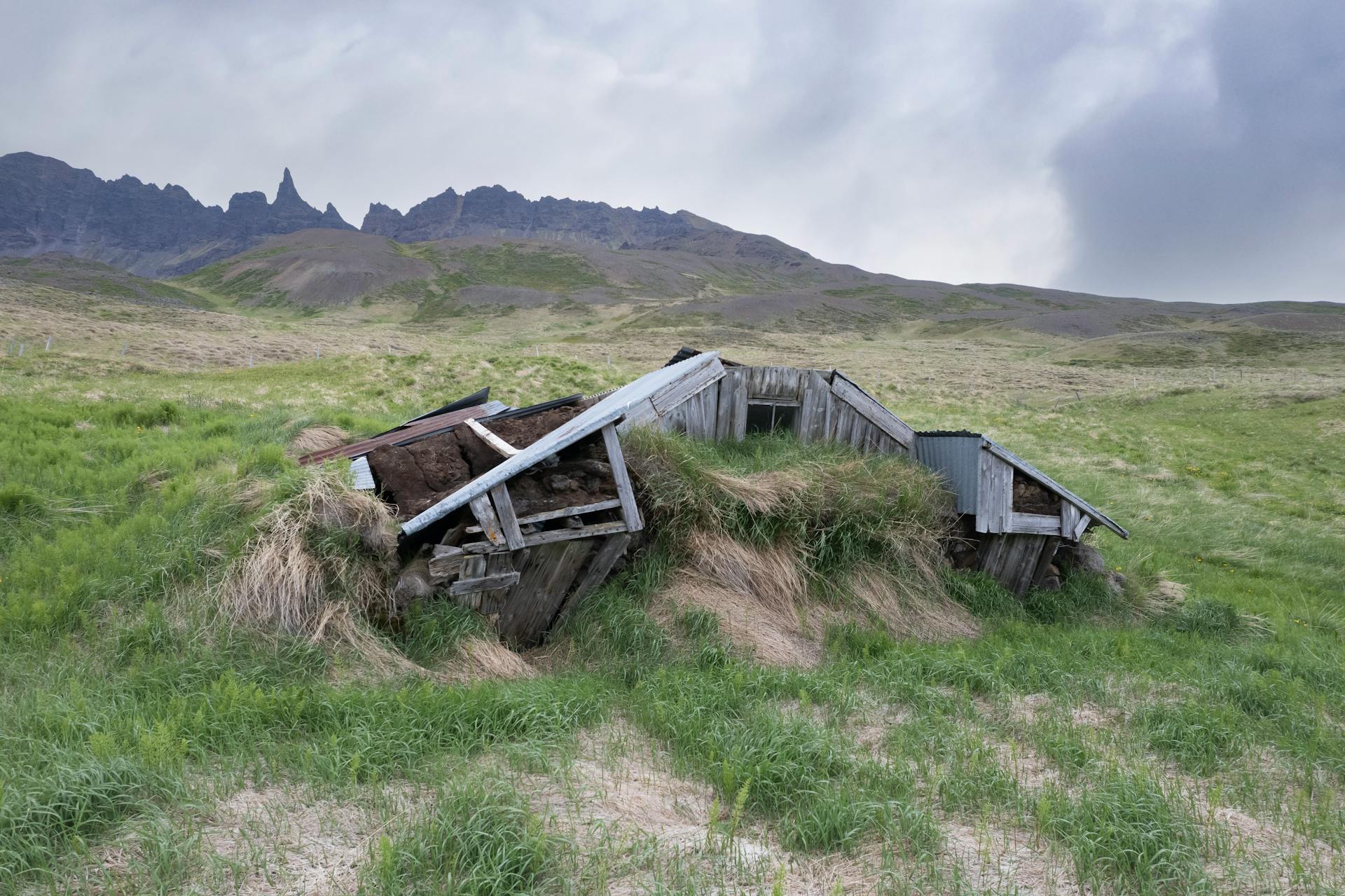 An old turf roof house in the scenic Icelandic countryside surrounded by mountains and open fields.