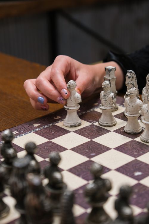 Free A woman's hand strategically moving a chess piece on a detailed chessboard. Focus on strategy and concentration. Stock Photo