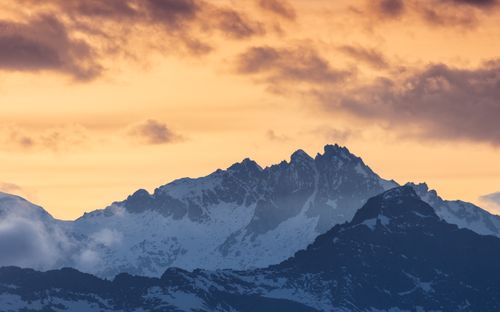Free Captivating image of snowy mountain peaks silhouetted against a golden sunset sky with dramatic clouds. Stock Photo