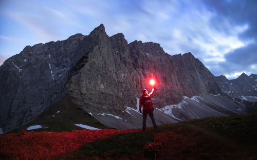Free A lone hiker holds a red flare against a majestic alpine backdrop at twilight. Stock Photo