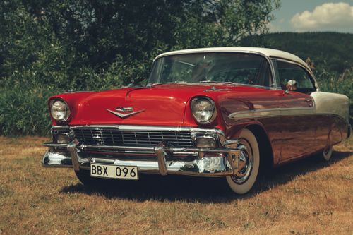 Free A vintage red Chevrolet car parked in a sunny rural area in Sweden, showcasing classic automobile design. Stock Photo