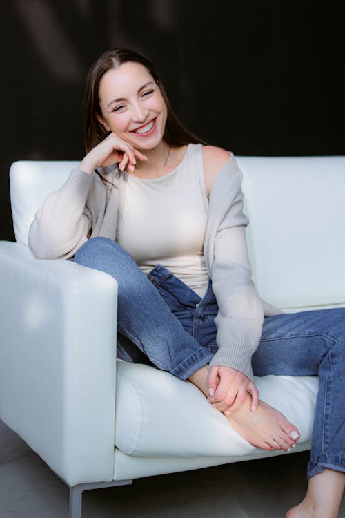 Model Wearing a Beige Tank Top and Blue Jeans Sitting on a White Sofa