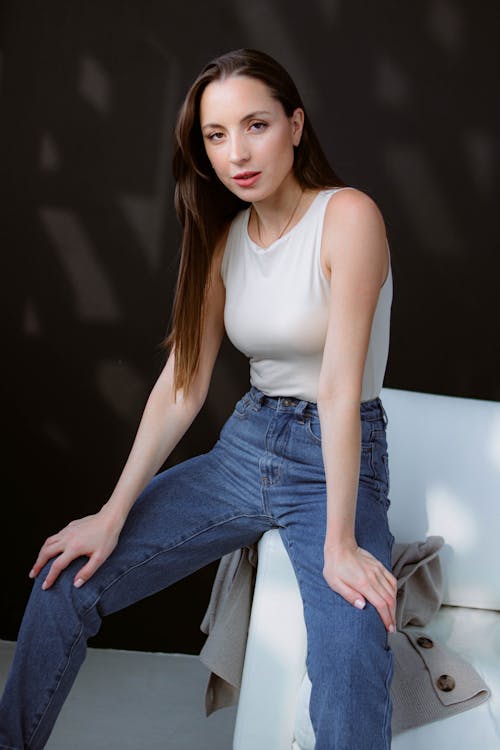 Model Wearing a Beige Tank Top and Blue Jeans Sitting on a White Sofa