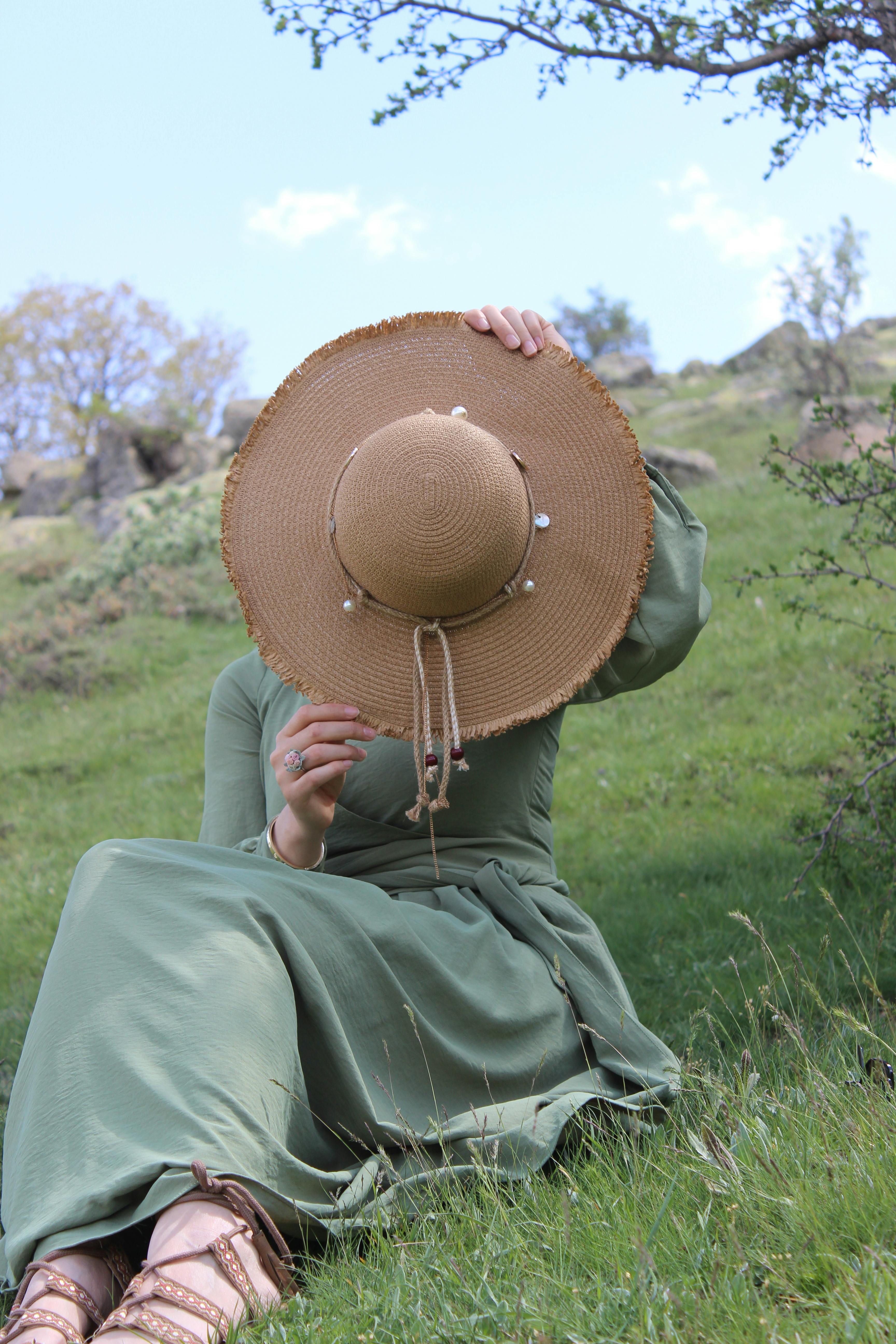 woman in hat and green dress sitting on grassland