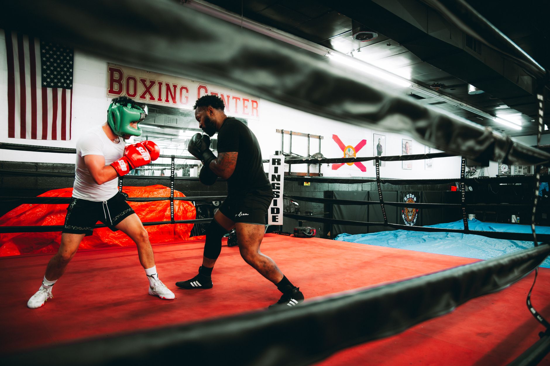 Intense boxing session between two men in a professional gym setting, showcasing athleticism and competition.