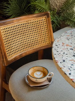 A beautifully crafted coffee cup with latte art on a rustic chair beside a terrazzo table.