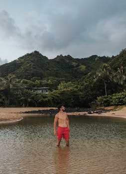 A man stands in a peaceful lagoon in Hawaii, surrounded by lush mountains and greenery.