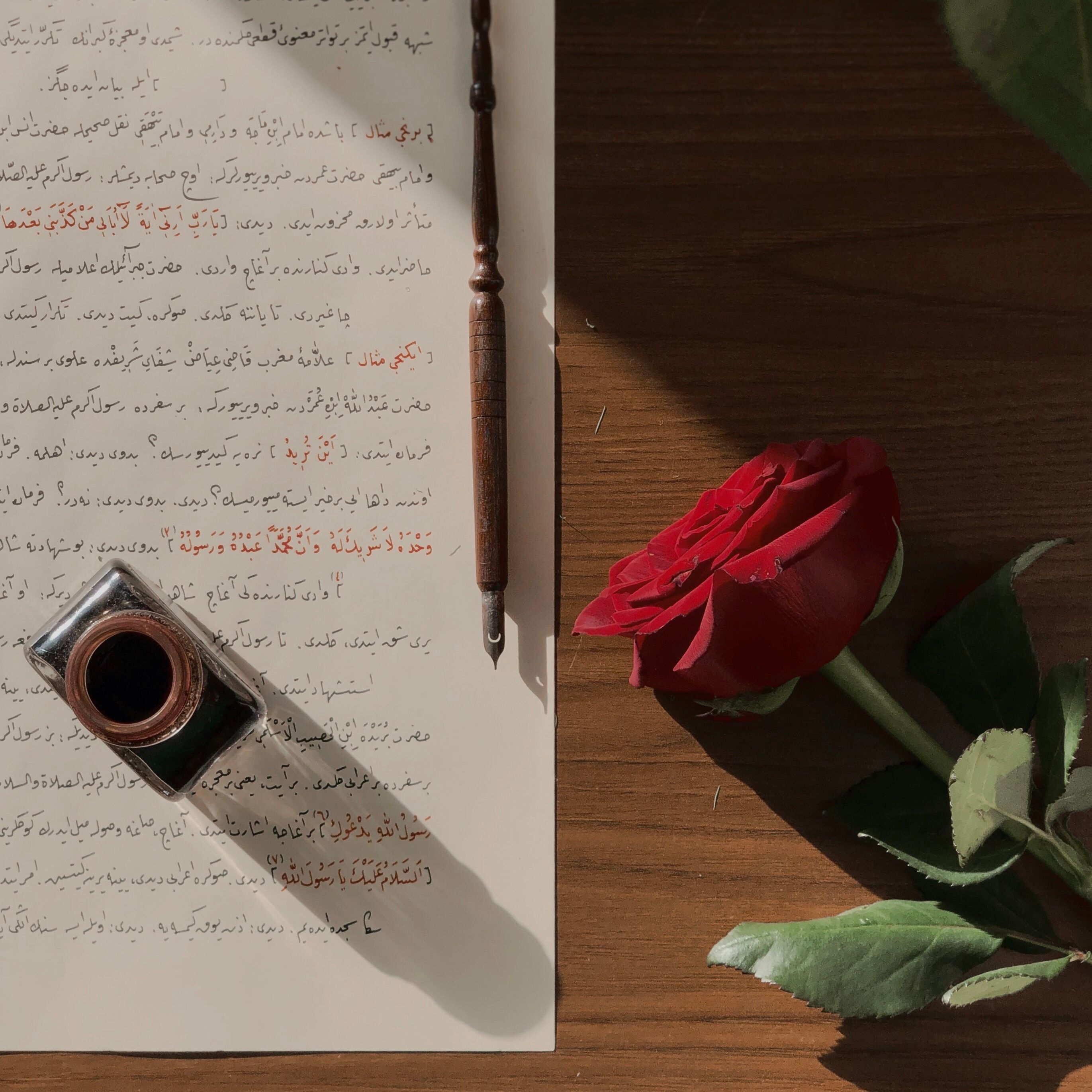 Elegant calligraphy with red rose and ink pen on wooden table, perfect for artistic themes.