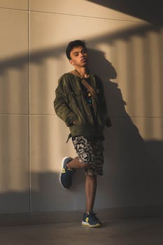 Stylish man posing against a white wall with dramatic shadows in urban setting.