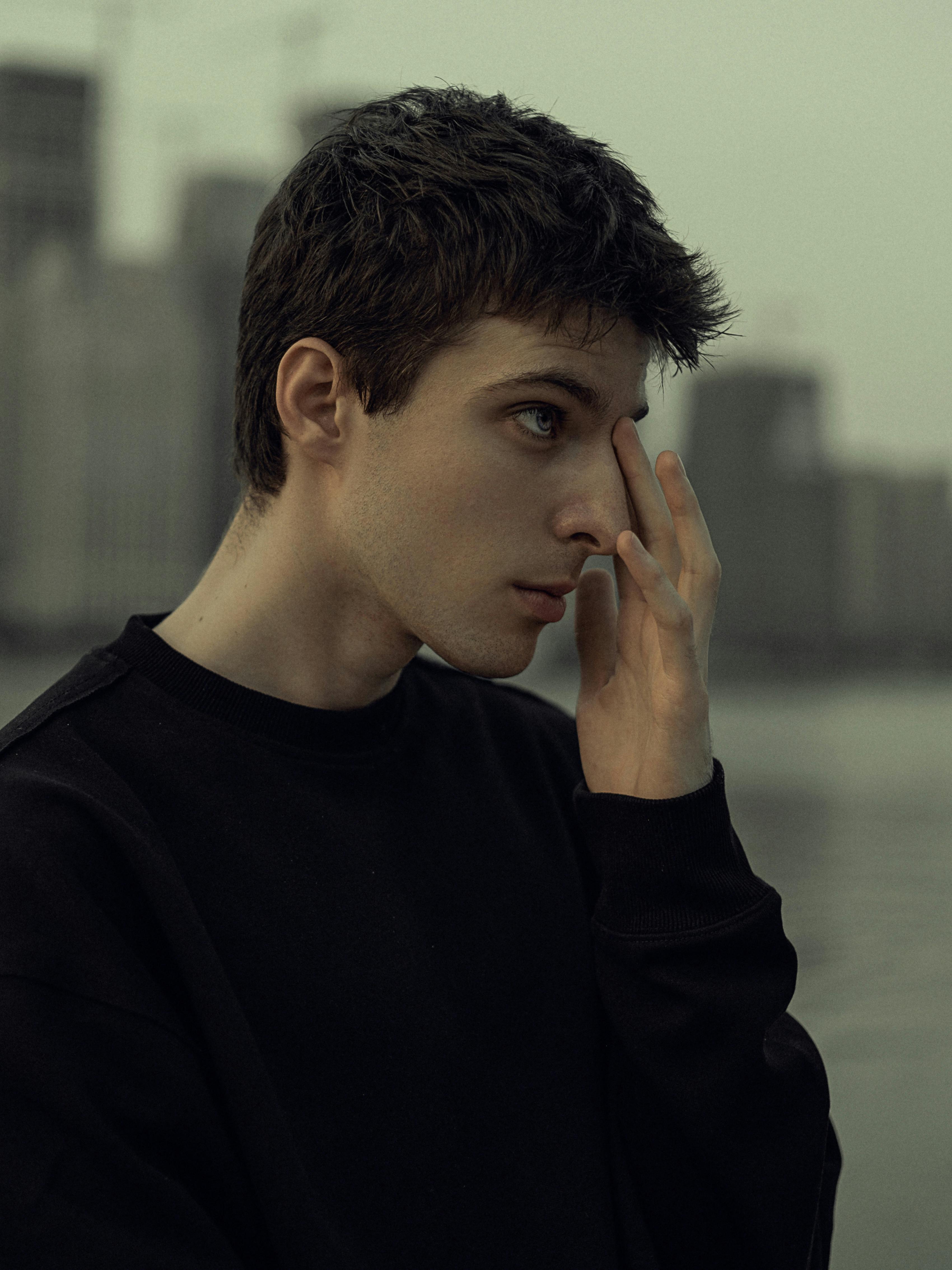 A profile shot of a young man in deep thought by the waterfront during dusk, exuding an introspective mood.