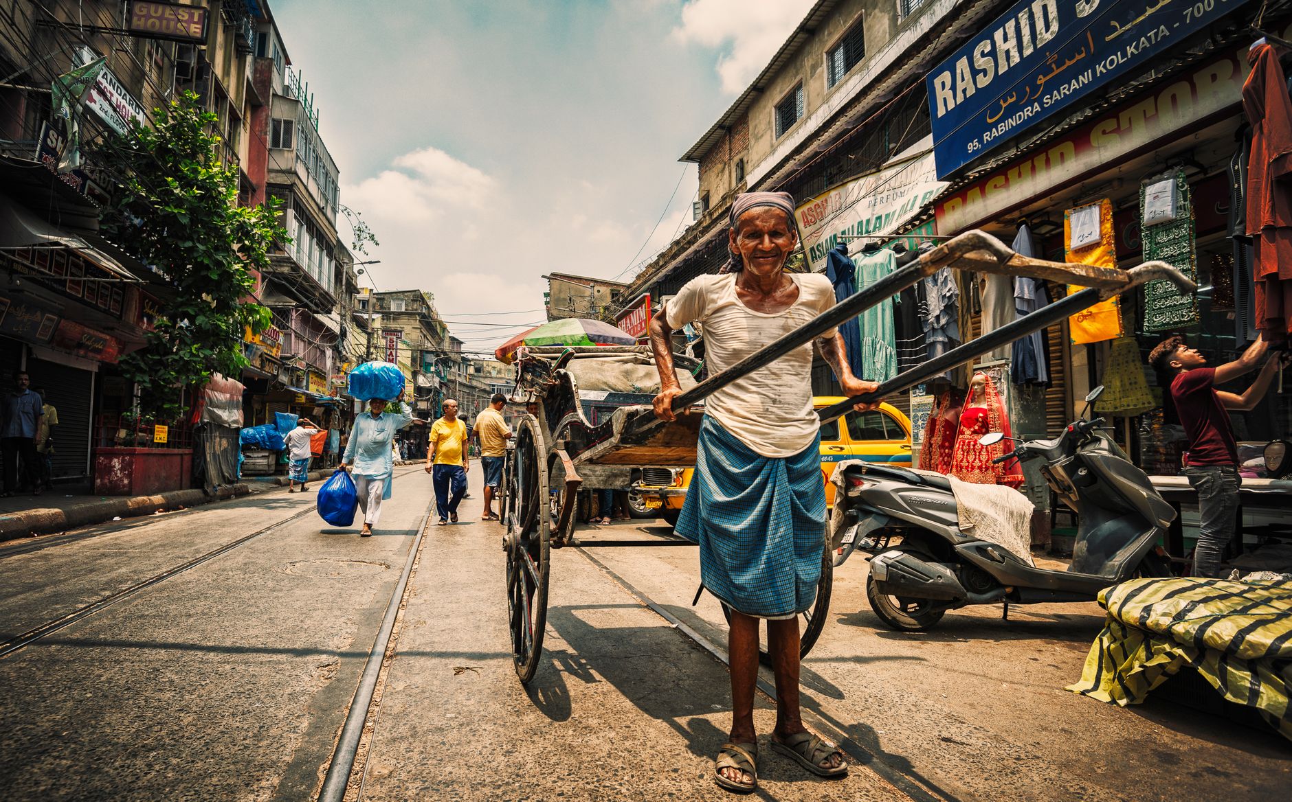 An elderly man pulls a rickshaw on a bustling street in Kolkata, showcasing urban life in India.