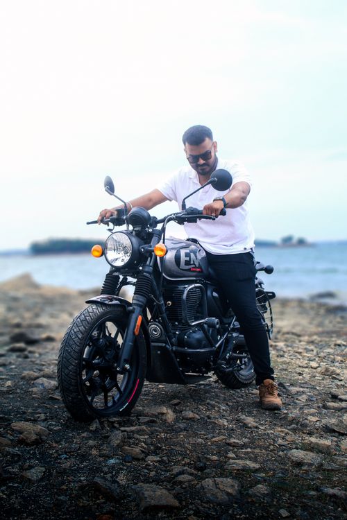 Free A man in sunglasses sits on a motorcycle by the beach, embodying a casual summer vibe. Stock Photo