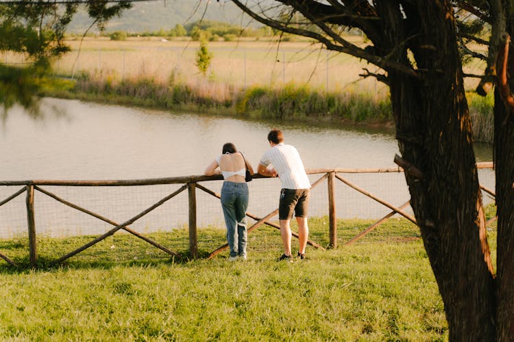 Back View Of A Man And Woman Standing By A Body Of Water 