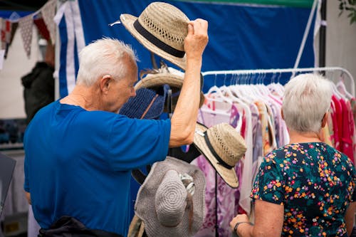 Elderly Man Trying on a Hat at a Clothing Market