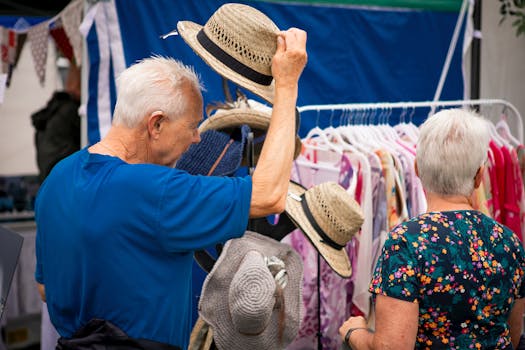 Senior couple browsing clothes and hats at an outdoor market stall during summer.