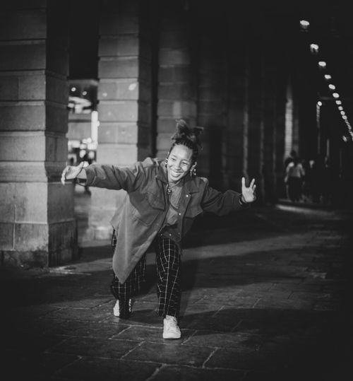 Free Black and white photo of a happy woman dancing on a city sidewalk at night. Stock Photo