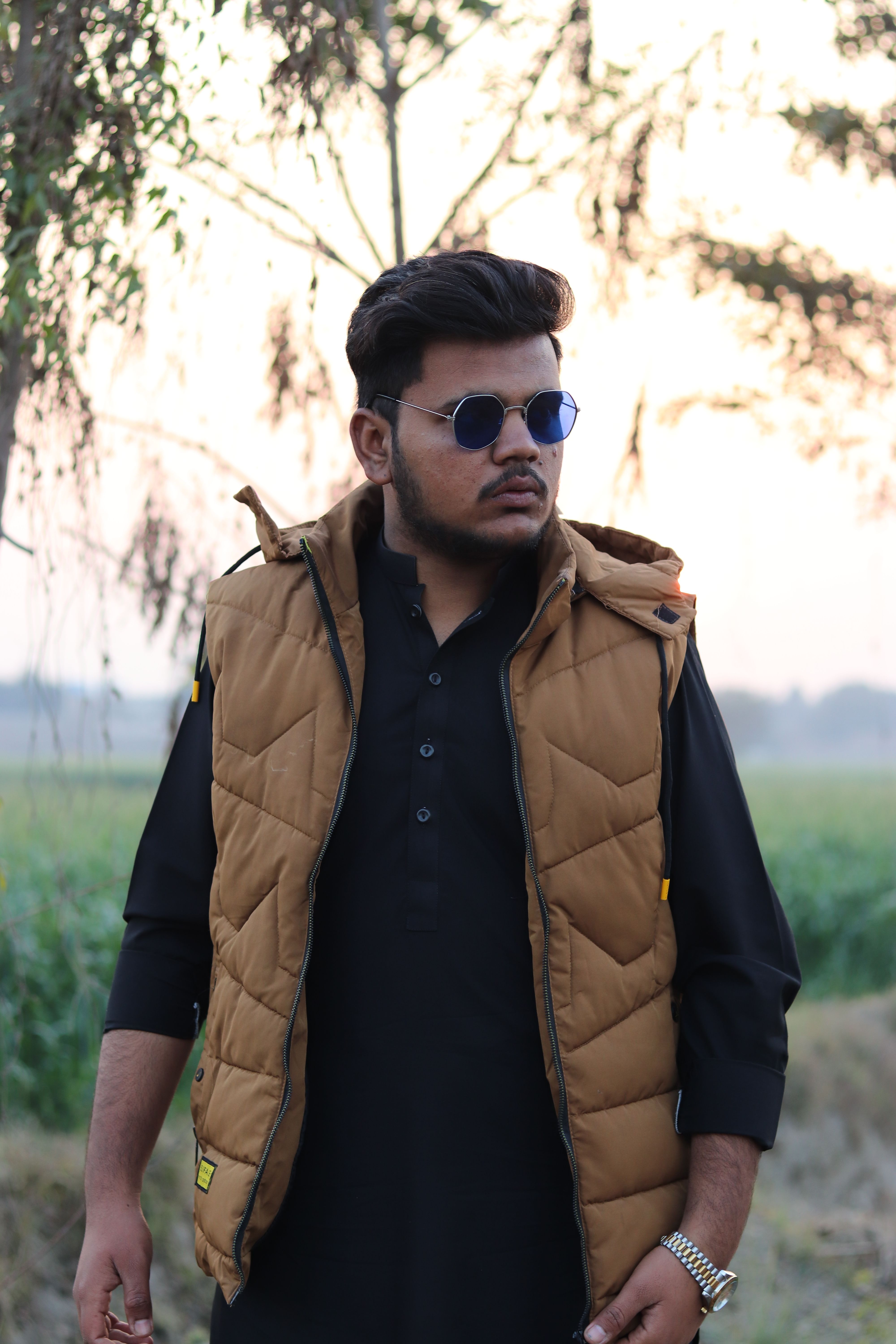 Portrait of a fashionable man in sunglasses and vest, posing outdoors.