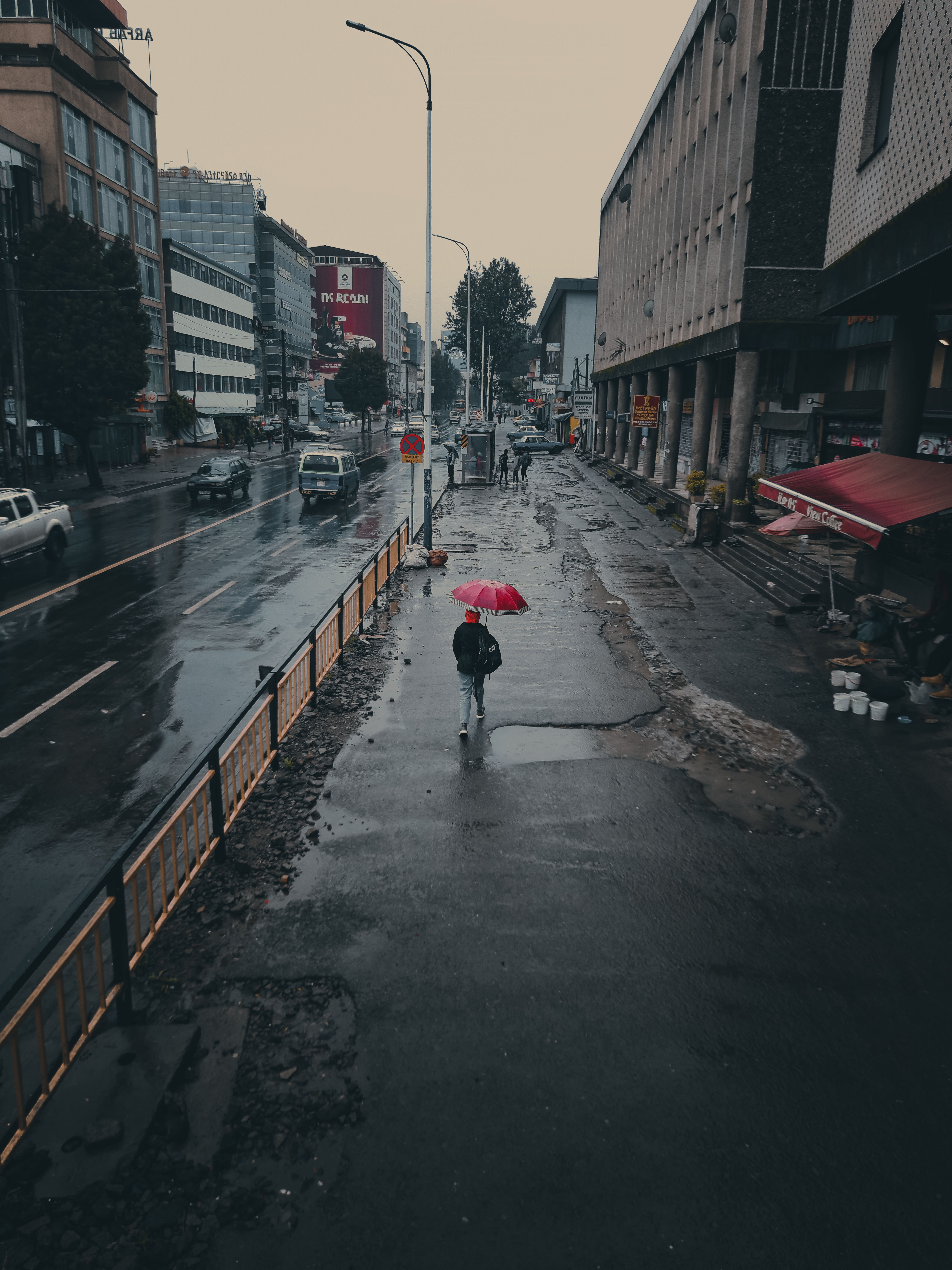 A solitary figure with a red umbrella walking along rainy city street in Addis Ababa, Ethiopia.