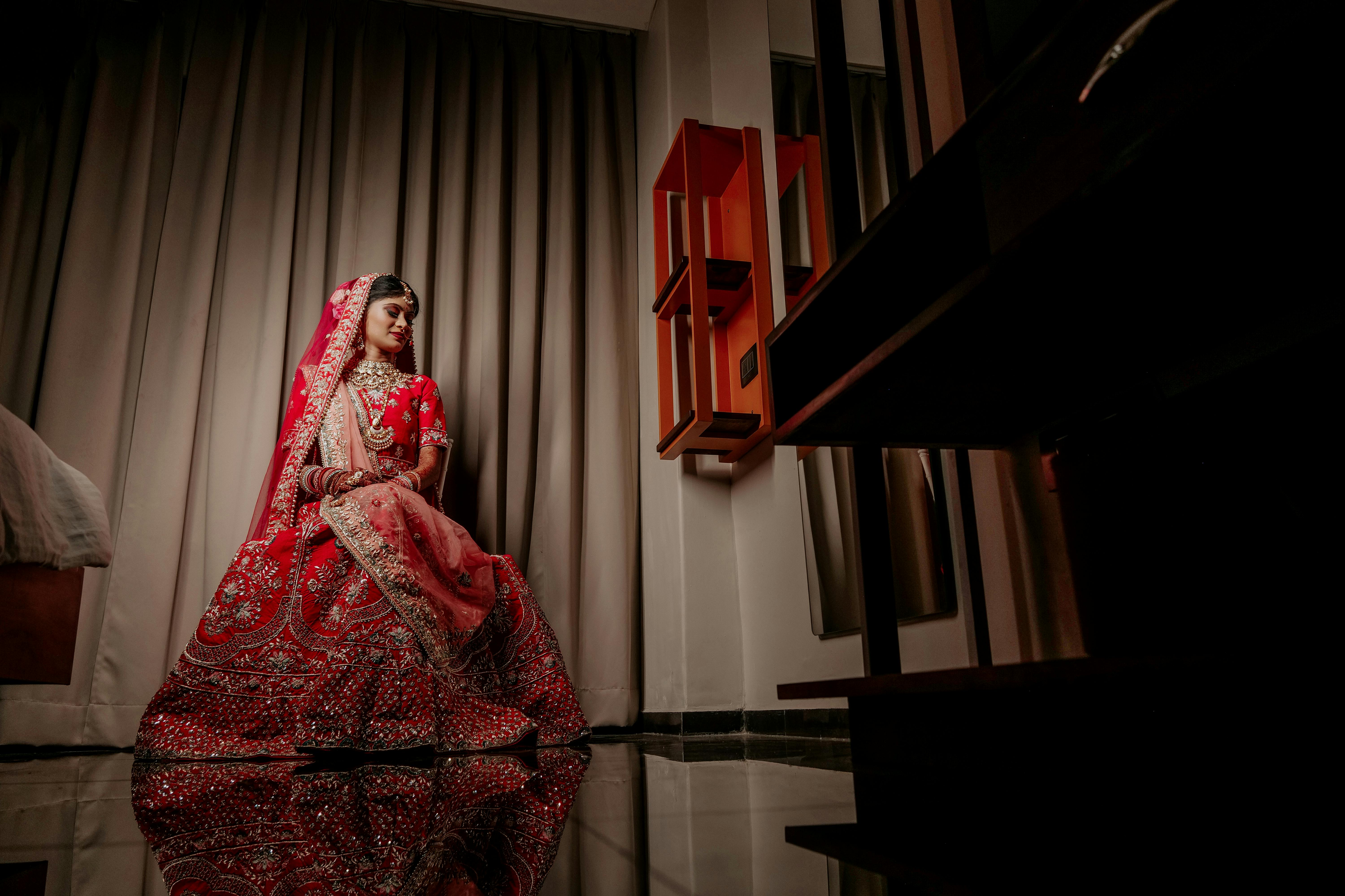 Beautiful Indian bride posing indoors in a stunning red lehenga, showcasing traditional clothing and fashion.