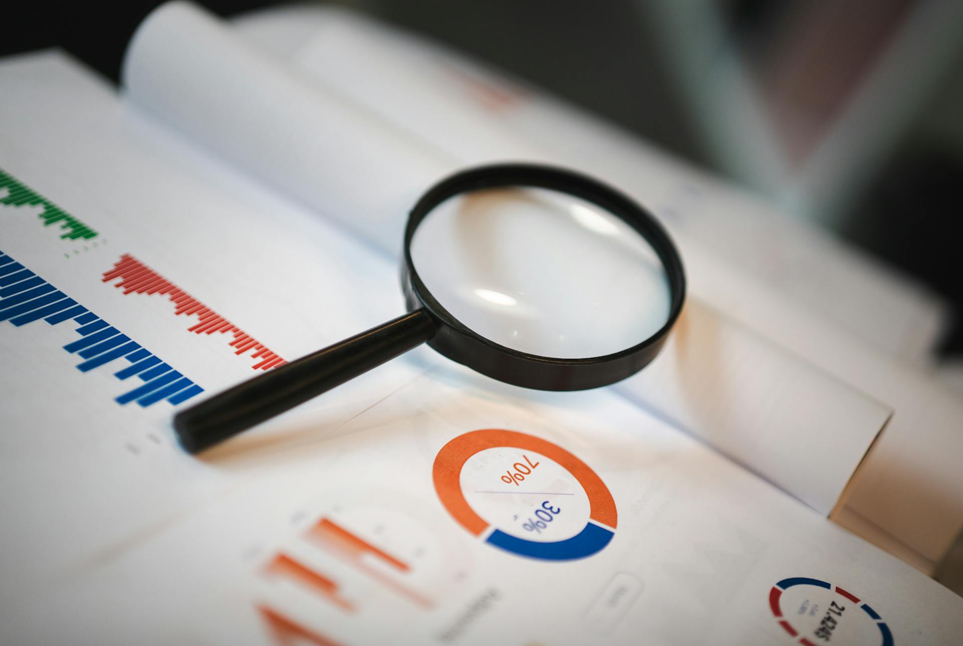 An image showcasing a magnifying glass placed on financial graphs and charts depicting statistical data.