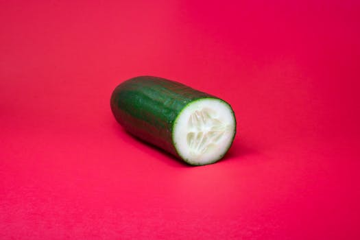 A vibrant studio shot of a sliced cucumber against a bold red backdrop, perfect for food photography.