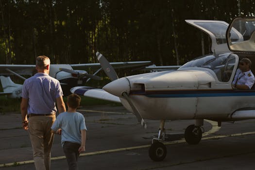 A man and child walk towards a small airplane with a pilot seated inside at an airport.
