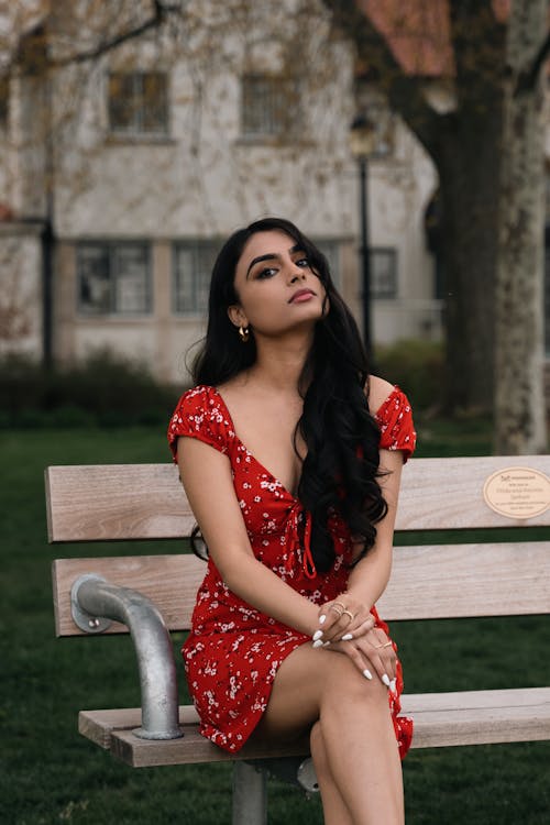 Beautiful Woman in a Red Floral Dress Sitting on a Bench 