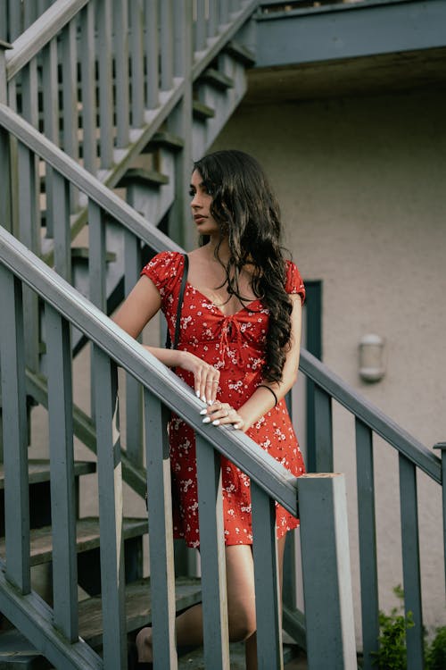 Woman in a Red Floral Dress Standing on the Stairs 