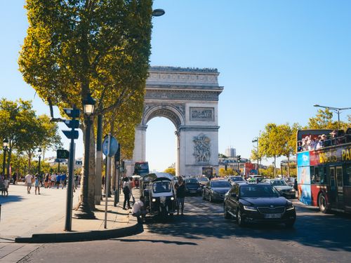 Free Bustling street scene at the Arc de Triomphe, Paris, featuring tourists and city traffic on a sunny day. Stock Photo