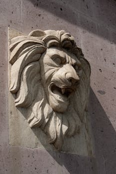A detailed stone lion sculpture carved on an exterior wall, captured in sunlight.