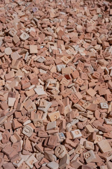 Close-up of piled clay tiles with engraved letters and numbers in an outdoor setting under bright light.