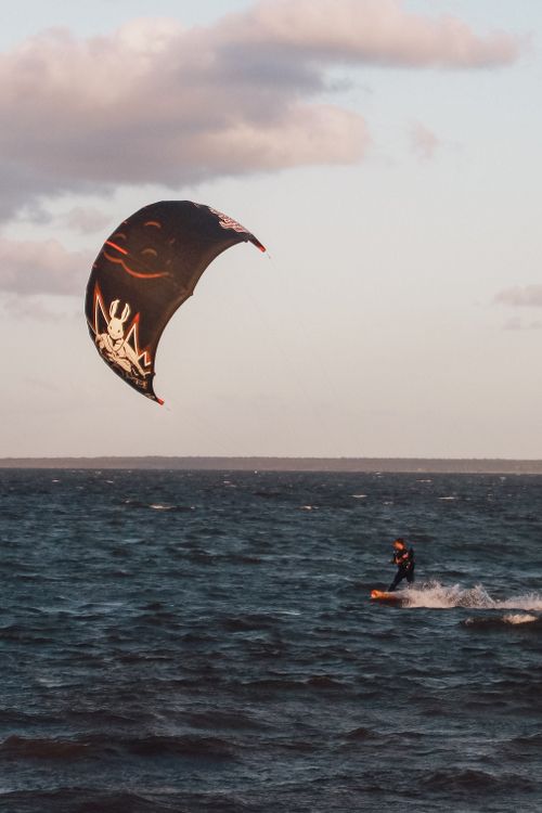 Free Kitesurfer rides waves under a vibrant sky in an exhilarating sea adventure. Stock Photo