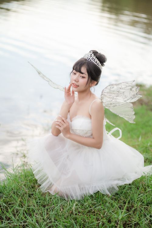 Free A whimsical portrait of a fairy-like woman in a serene natural setting by the water. Stock Photo