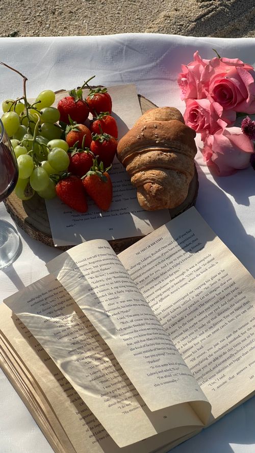 Free A stylish picnic setup featuring grapes, strawberries, a croissant, and a book. Stock Photo