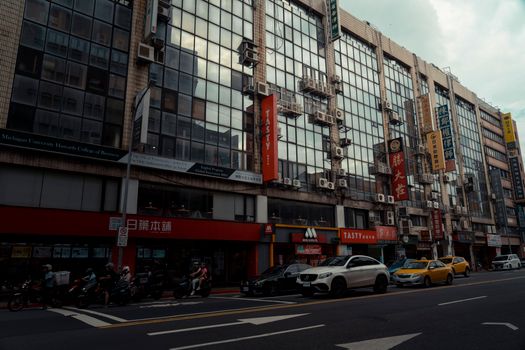 Street view of modern buildings in Taipei with traffic and reflective glass facades.