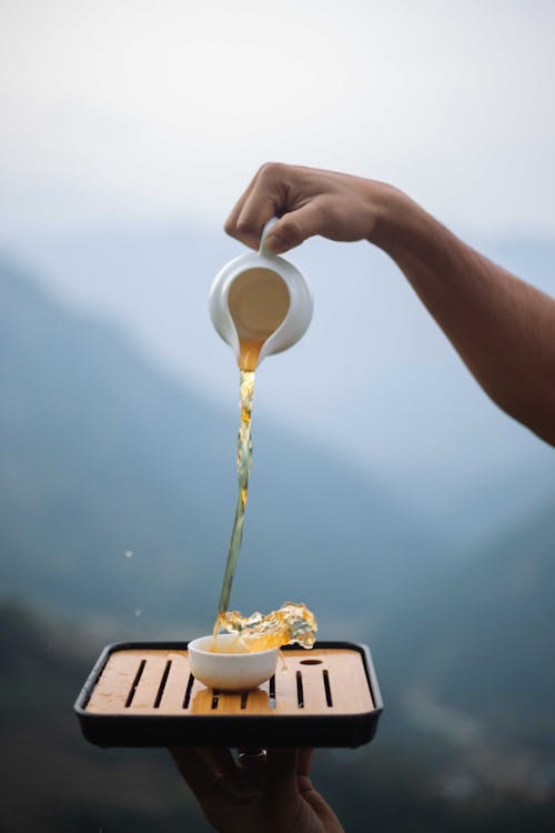 Hand Holding Pitcher and Pouring Tea to Cup