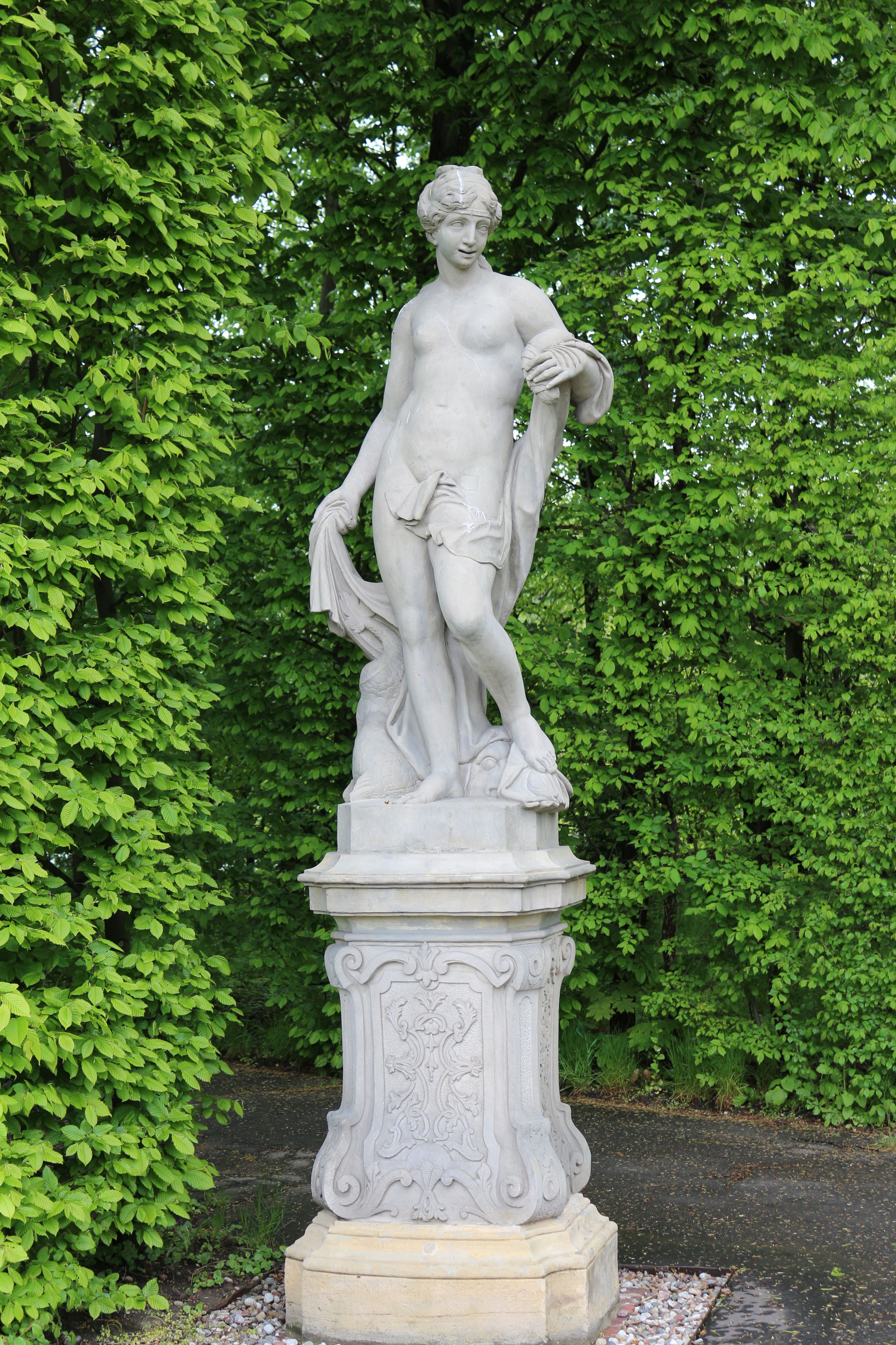Marble statue in lush greenery at Wilanów Park, Świętokrzyskie Voivodeship, Poland.