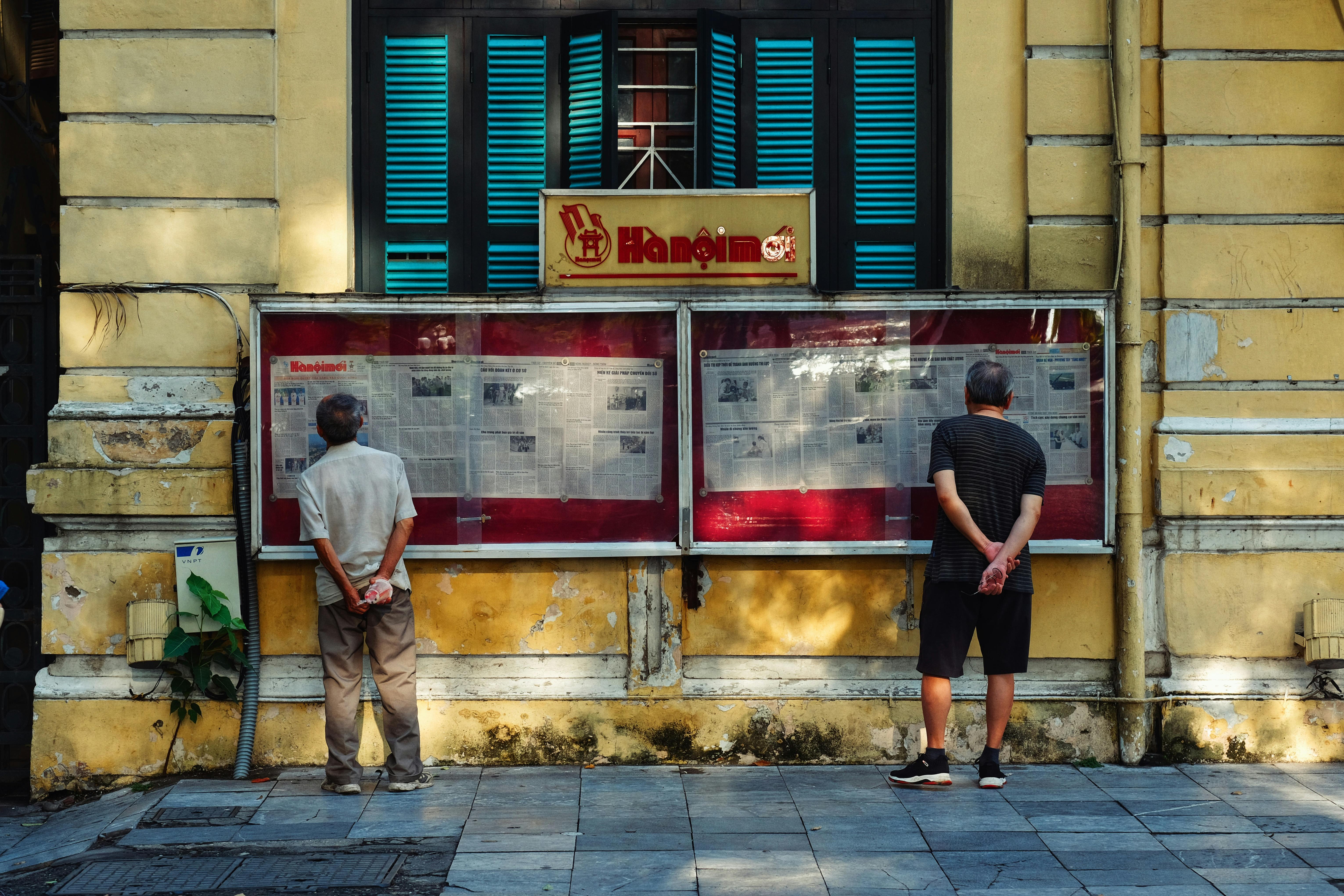 men reading news in the paper hung in a cabinet on the street