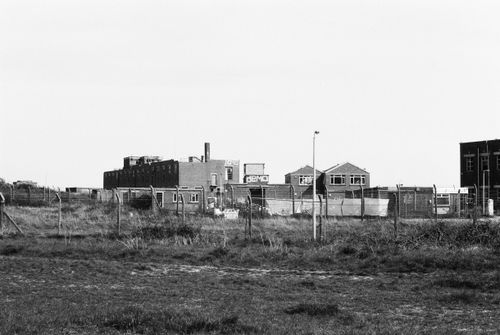 Free Black and white photo of an abandoned industrial complex with a fence in the foreground. Stock Photo