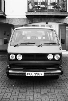 Classic black and white photo of a vintage Volkswagen van parked in an urban environment.