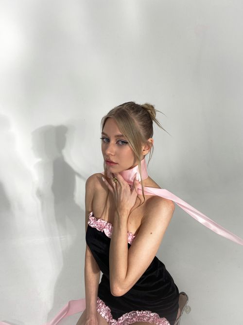 Free Stylish model in a black nightgown with pink accents, posing with a ribbon in a studio setting. Stock Photo